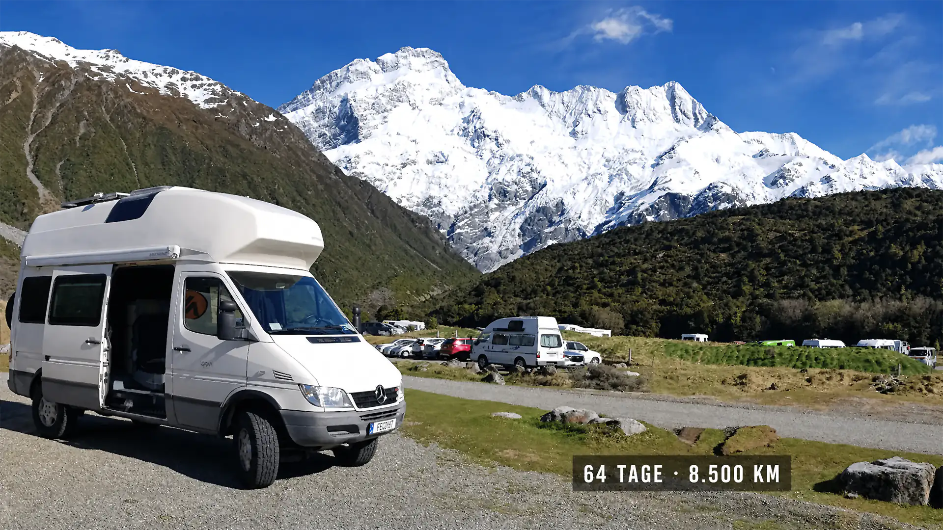 Weißer James-Cook-Camper mit geöffneter Seitentür vor schneebedeckter Bergkette in Neuseeland