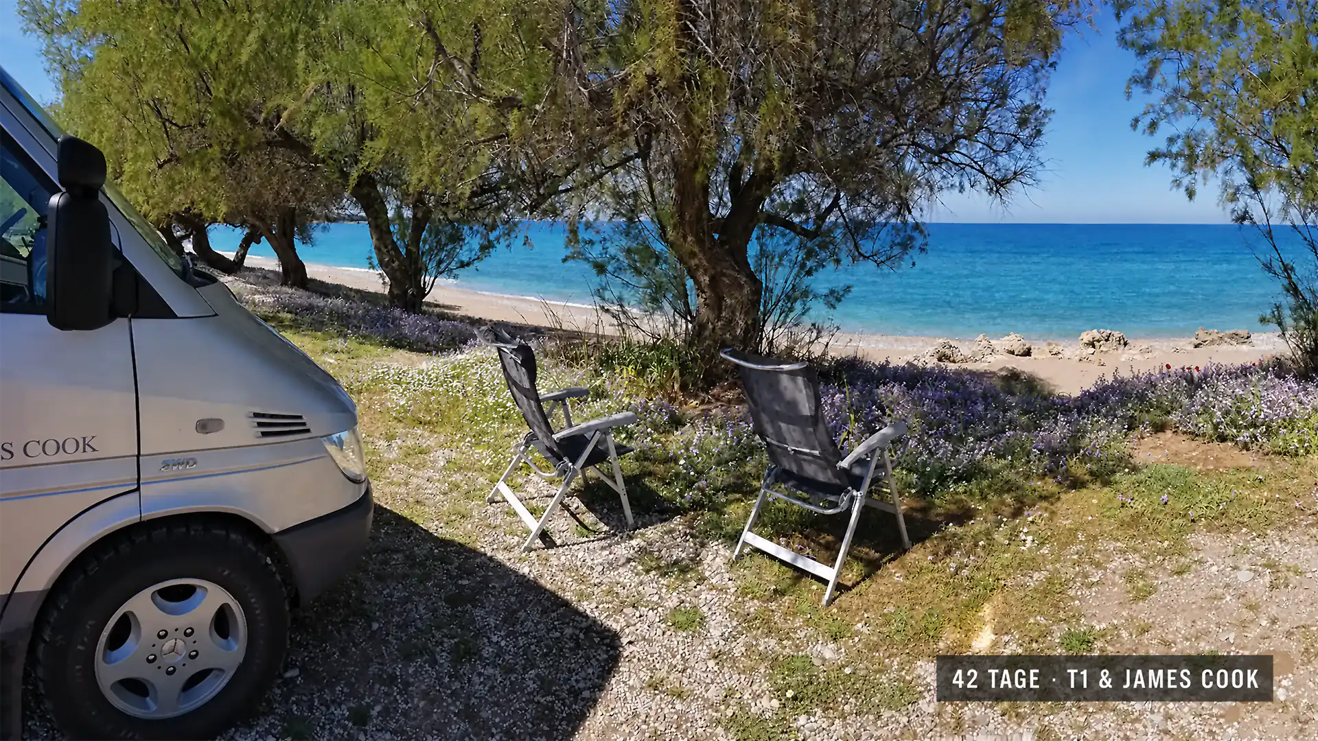 James-Cook-Camper und zwei Campingstühle unter Bäumen an türkisfarbener Meeresbucht auf dem Peloponnes