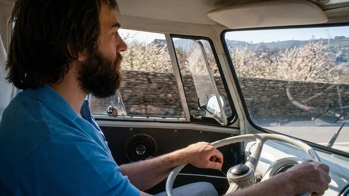 Fahrer am Steuer eines klassischen VW T1 während einer Fahrt durch eine ländliche Umgebung